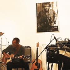 Martin Fly spiller guitar på scenen og der er en Jimmy Hendrix plakat på væggen.